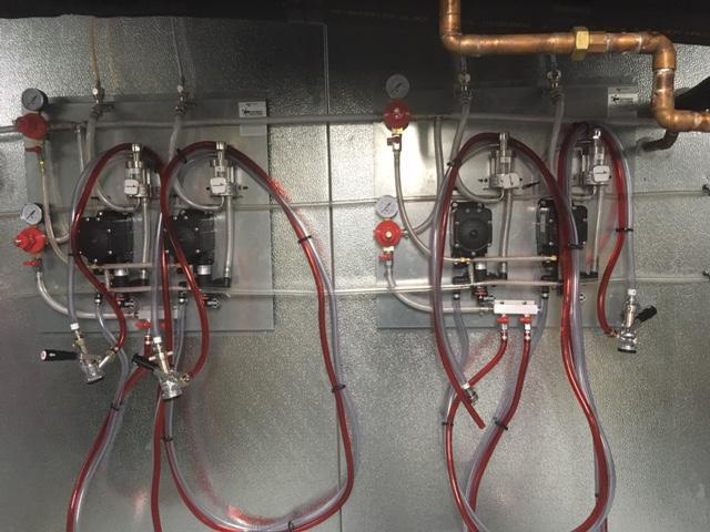 Two sets of gauges, tubes, and valves are mounted on a metallic wall, interconnected with red and transparent pipes.